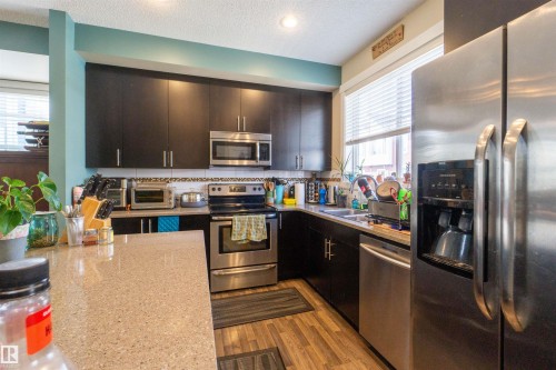Kitchen featuring dark cabinetry, light-colored countertops, stainless steel appliances, and wood-finish flooring - #75 8315 180 Av Nw, Edmonton, AB 