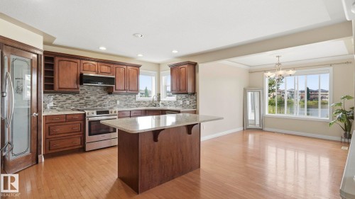 Open-concept kitchen featuring wood-finish flooring, dark wood cabinetry, stainless steel appliances, a tiled backsplash, and a central island with a light-colored countertop - 6116 53 Avenue, Beaumont, AB - Indoor Photo Showing Kitchen With Upgraded Kitchen