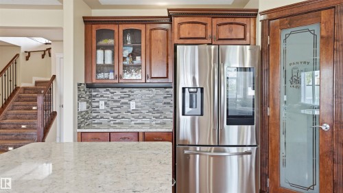 Kitchen featuring a stainless steel refrigerator, wood cabinetry with glass-front uppers, a mosaic tile backsplash, and a light-toned countertop - 6116 53 Avenue, Beaumont, AB - Indoor Photo Showing Other Room