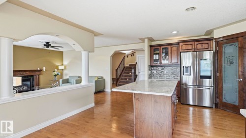 Spacious kitchen with a central island featuring a light-toned countertop, stainless steel refrigerator, and dark wood cabinetry with glass-front accents - 6116 53 Avenue, Beaumont, AB - Indoor Photo Showing Kitchen