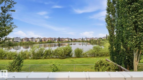Expansive waterfront property featuring a large body of water, lush green lawn, mature trees, and a distant residential area - 6116 53 Avenue, Beaumont, AB - Outdoor With View