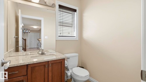 Bathroom featuring a wood-finish vanity with a light-toned countertop, an integrated sink, and a large wall-mounted mirror - 6116 53 Avenue, Beaumont, AB - Indoor Photo Showing Bathroom