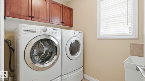 Dedicated laundry space featuring rich wood-finish cabinetry, a window with horizontal blinds, and a built-in utility sink with tile backsplash - 6116 53 Avenue, Beaumont, AB - Indoor Photo Showing Laundry Room