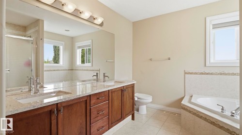 Bathroom featuring a double vanity with stone countertops, wood-finish cabinetry, and an expansive mirror - 6116 53 Avenue, Beaumont, AB - Indoor Photo Showing Bathroom