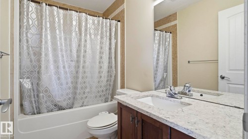 Bathroom featuring a white bathtub, ceramic tile surround, and a vanity with a light-colored countertop and dark wood-finish cabinetry - 6116 53 Avenue, Beaumont, AB - Indoor Photo Showing Bathroom