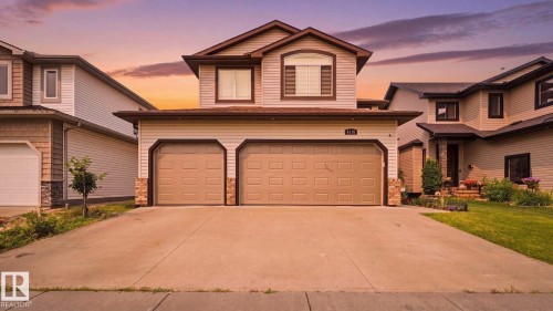 Two-story residence featuring light-colored siding, a prominent two-car garage with panel doors, and a spacious concrete driveway - 6116 53 Avenue, Beaumont, AB - Outdoor