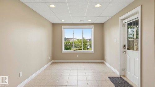 Spacious room featuring neutral paint, light tile flooring, a window offering exterior scenery, recessed lighting, and a white paneled door with a half-light insert - 6116 53 Avenue, Beaumont, AB - Indoor Photo Showing Other Room