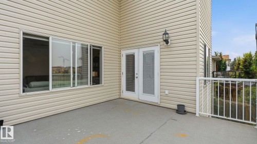 Exterior patio with light beige horizontal siding, white double French doors, large sliding window, white metal railing, and an exterior wall lantern - 6116 53 Avenue, Beaumont, AB - Outdoor With Exterior