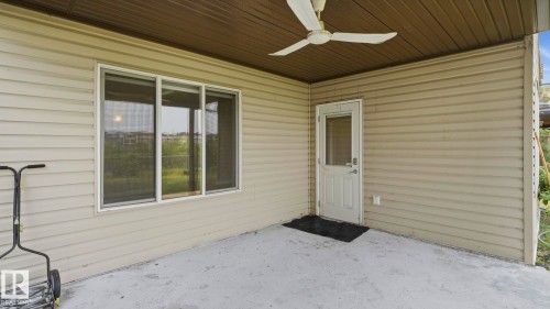 Covered patio featuring a ceiling fan, light beige vinyl siding, a white exterior door with glass insert, and a three-panel window - 6116 53 Avenue, Beaumont, AB - Outdoor With Exterior