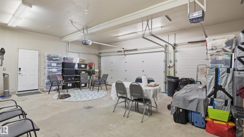 Spacious garage featuring concrete flooring, overhead lighting, and two white overhead doors - 6116 53 Avenue, Beaumont, AB - Indoor Photo Showing Garage