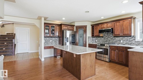 Open-concept kitchen featuring wood-finish flooring, a central island with a light-toned countertop, stainless steel appliances, and a mosaic tile backsplash - 6116 53 Avenue, Beaumont, AB - Indoor Photo Showing Kitchen With Stainless Steel Kitchen With Double Sink With Upgraded Kitchen