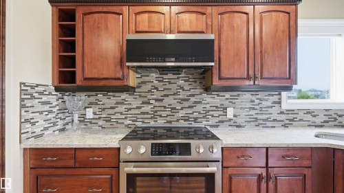 Kitchen featuring wood cabinetry, stainless steel range with microwave oven, stone-finish countertops, and a mosaic tile backsplash - 6116 53 Avenue, Beaumont, AB - Indoor Photo Showing Kitchen