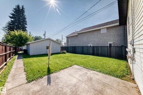 Expansive grassy yard with concrete patio, chain-link fencing, and detached garage - 12721 117 Street Nw, Edmonton, AB 
