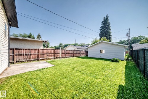 Expansive green lawn with a concrete patio, wood privacy fencing, and a detached white siding garage - 12721 117 Street Nw, Edmonton, AB 