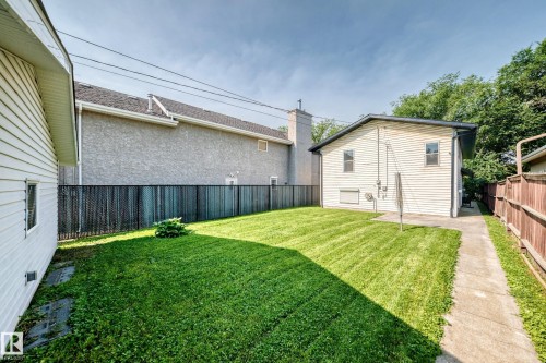 Expansive grass lawn with concrete side path, vertical plank fencing, and horizontal siding exterior - 12721 117 Street Nw, Edmonton, AB 