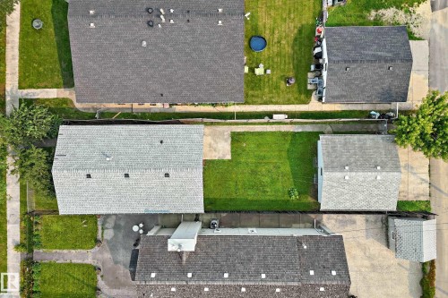 Property with two distinct rooflines, featuring a substantial grassy area, a concrete pad, and mature trees - 12721 117 Street Nw, Edmonton, AB 