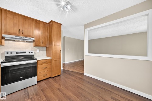 Stainless steel range with coordinating ventilation hood, wood-finish cabinetry, light-toned countertop, and wood-finish flooring - 12721 117 Street Nw, Edmonton, AB 