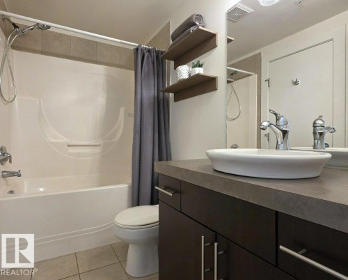 Bathroom featuring a combined shower and tub, tile flooring, a vessel sink, a dark wood-finish vanity, and wall-mounted shelving - #605 10152 104 St Nw, Edmonton, AB 