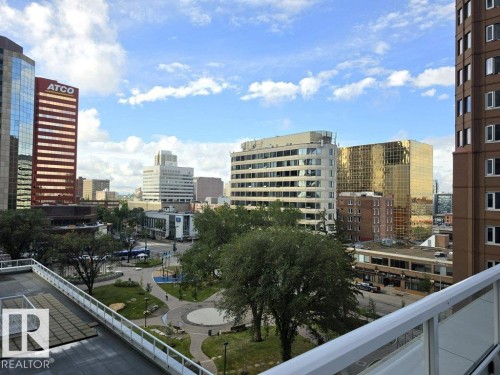 Urban cityscape with varied architectural styles, a public park with mature trees and pathways, and a building with a glass railing balcony - #605 10152 104 St Nw, Edmonton, AB 