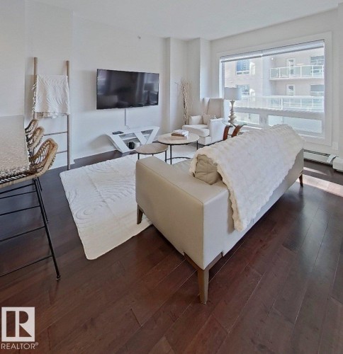 Expansive dark wood-finish flooring, large window with roller shades, white wall finishes, and a contemporary media console - #605 10152 104 St Nw, Edmonton, AB 