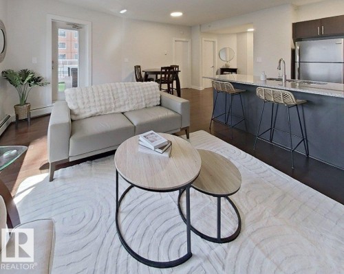 Open concept living area featuring dark wood-finish flooring, a kitchen island with seating, stainless steel appliances, and a glass-paneled exterior door - #605 10152 104 St Nw, Edmonton, AB 