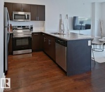 Kitchen featuring wood-finish flooring, stainless steel appliances, dark wood-finish cabinetry, and a light-toned countertop - 