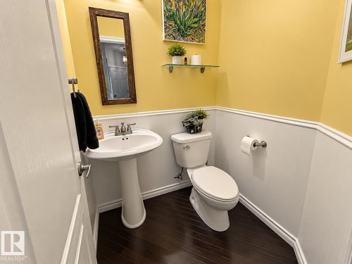 Pedestal sink with a dual-handle faucet, wood-finish flooring, white wainscoting, and a wall-mounted glass shelf - 16893 58A Street Nw, Edmonton, AB 