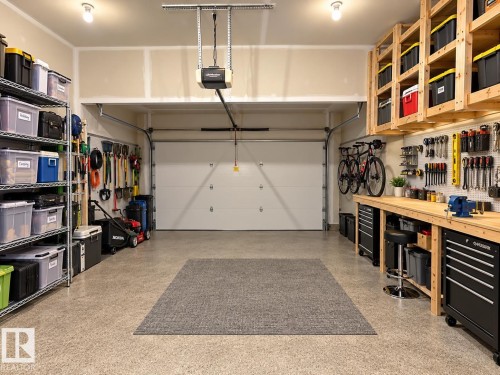 Spacious garage with an automatic overhead door, built-in wooden shelving, a workbench, and durable epoxy flooring - 16893 58A Street Nw, Edmonton, AB 