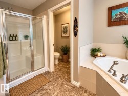 Walk-in shower with clear glass enclosure and chrome hardware, corner soaking tub with deck-mounted fixtures, and textured flooring - 
