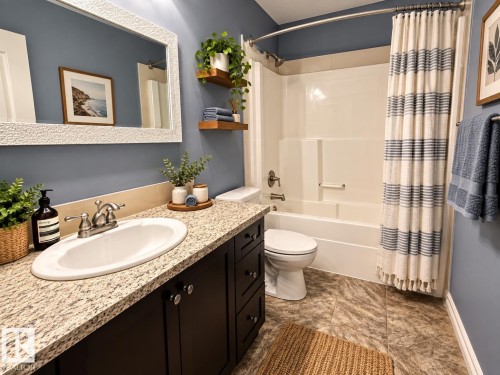 Granite-look countertop, undermount sink, dark wood-finish cabinetry, built-in bathtub, and wood-look flooring - 16893 58A Street Nw, Edmonton, AB 