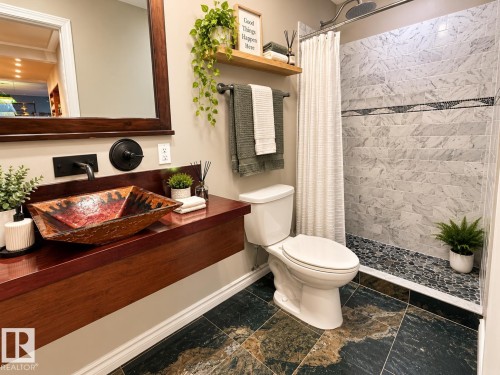 Custom vessel sink, wood-finish floating vanity, wall-mounted faucet, floor-to-ceiling tiled shower, and a rain showerhead - 16893 58A Street Nw, Edmonton, AB 