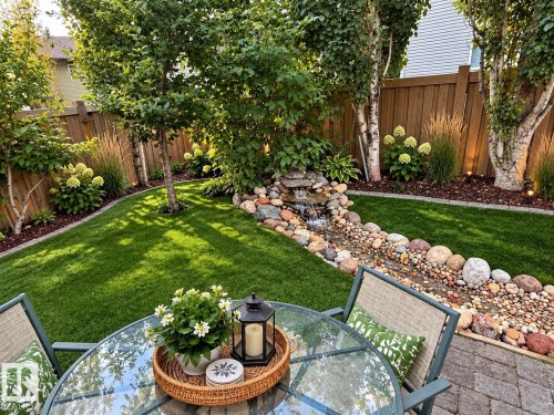 Expansive backyard featuring a manicured lawn, a rock-lined stream with a waterfall, mature trees, and a privacy fence - 16893 58A Street Nw, Edmonton, AB 