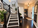 Two-story foyer featuring dark wood-finish flooring, a grand staircase with wrought iron spindles, a front entry door with a sidelight, and an integrated built-in bench with hooks - 16893 58A Street Nw, Edmonton, AB 
