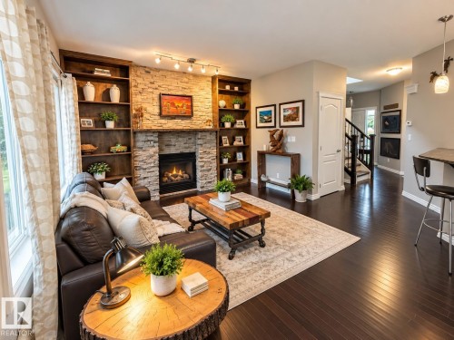 Stone-clad fireplace with a gas insert, dark wood built-in shelving, dark wood-finish flooring, white trim, and a white interior door - 16893 58A Street Nw, Edmonton, AB 
