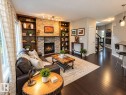 Stone-clad fireplace with a gas insert, dark wood built-in shelving, dark wood-finish flooring, white trim, and a white interior door - 16893 58A Street Nw, Edmonton, AB 