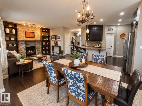 Stone-faced fireplace with hearth, built-in shelving, dark wood-finish flooring, and a chandelier - 16893 58A Street Nw, Edmonton, AB 