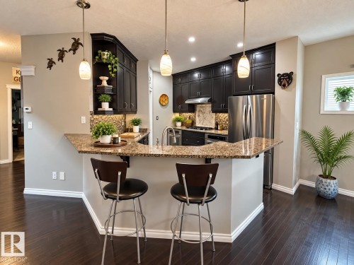 Kitchen with dark wood-finish cabinetry, stainless steel appliances, speckled stone countertops, and a mosaic tile backsplash - 16893 58A Street Nw, Edmonton, AB 