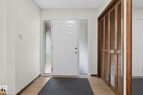 Entryway featuring a white paneled door with frosted sidelights, wood-finish flooring, and a louvered bi-fold closet - 12121 42 Street Nw, Edmonton, AB - Indoor Photo Showing Other Room
