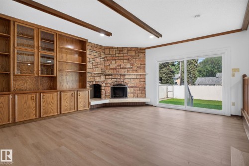 Spacious interior featuring wood-finish flooring, exposed ceiling beams, and a stone-clad fireplace - 12121 42 Street Nw, Edmonton, AB - Indoor With Fireplace
