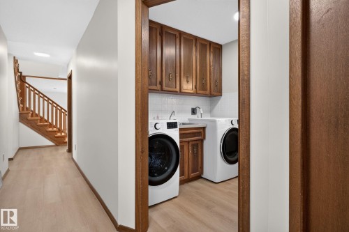 Dedicated laundry area featuring wood cabinetry, white subway tile backsplash, and a utility sink - 12121 42 Street Nw, Edmonton, AB - Indoor Photo Showing Laundry Room