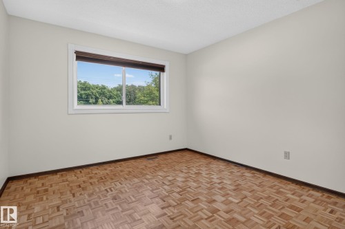 Parquet wood flooring and light-toned walls with a white trim window overlooking green foliage - 12121 42 Street Nw, Edmonton, AB - Indoor Photo Showing Other Room