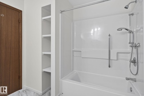 White bathtub and shower combination featuring a multi-function showerhead, an additional shower wand, and a chrome grab bar - 12121 42 Street Nw, Edmonton, AB - Indoor Photo Showing Bathroom