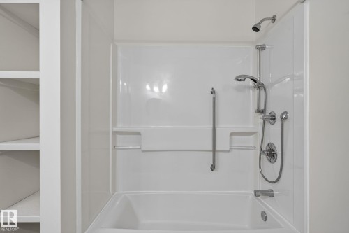 Bathtub and shower combination featuring a multi-function showerhead with a handheld spray, integrated shelving, and a grab bar - 12121 42 Street Nw, Edmonton, AB - Indoor Photo Showing Bathroom
