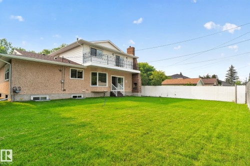 Expansive green lawn with a two-story residence featuring a stucco exterior and a second-story balcony with an ornate metal railing - 12121 42 Street Nw, Edmonton, AB - Outdoor