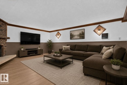 Spacious living area featuring a brick fireplace with a hearth, wood-finish flooring, and crown molding - 12121 42 Street Nw, Edmonton, AB - Indoor Photo Showing Living Room With Fireplace