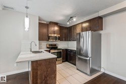 Kitchen featuring dark wood cabinetry, stainless steel appliances, white quartz countertops, and a white tile backsplash - 