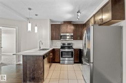 Modern kitchen featuring stainless steel appliances, dark wood-finish cabinetry, a white subway tile backsplash, and a breakfast bar with pendant lighting - 