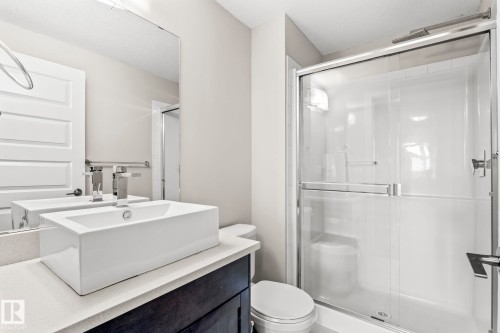 Modern bathroom featuring a rectangular vessel sink with a chrome faucet, light-toned countertop, dark wood-finish vanity, and a glass-enclosed shower with a sliding door - 5151 Windermere  Bv Sw, Edmonton, AB - Indoor Photo Showing Bathroom