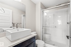 Modern bathroom featuring a rectangular vessel sink with a chrome faucet, light-toned countertop, dark wood-finish vanity, and a glass-enclosed shower with a sliding door - 