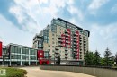 Contemporary multi-story building featuring a red and beige facade, multiple balconies with glass railings, and expansive glass window sections - 5151 Windermere  Bv Sw, Edmonton, AB  - Outdoor 